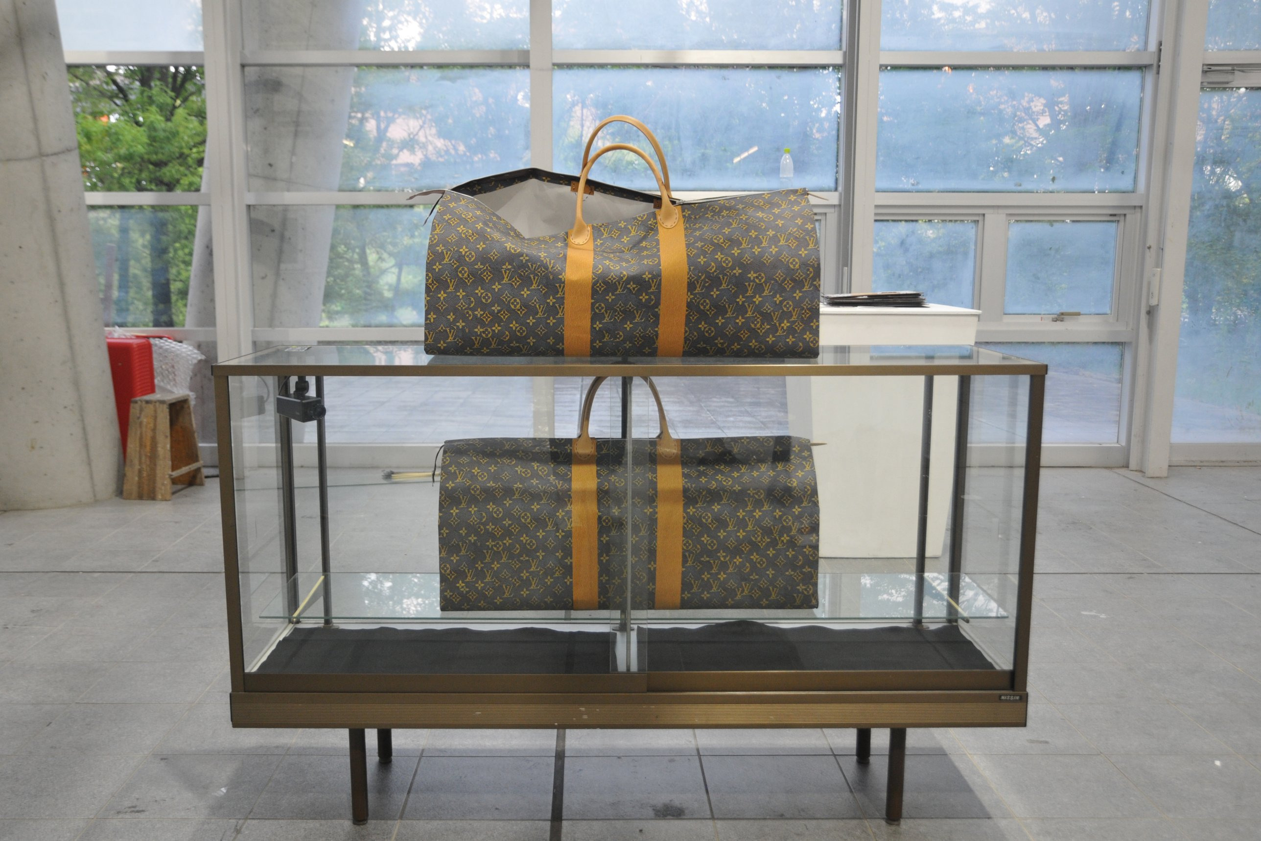 Two paper bags printed with a monogram pattern displayed on and inside a glass showcase