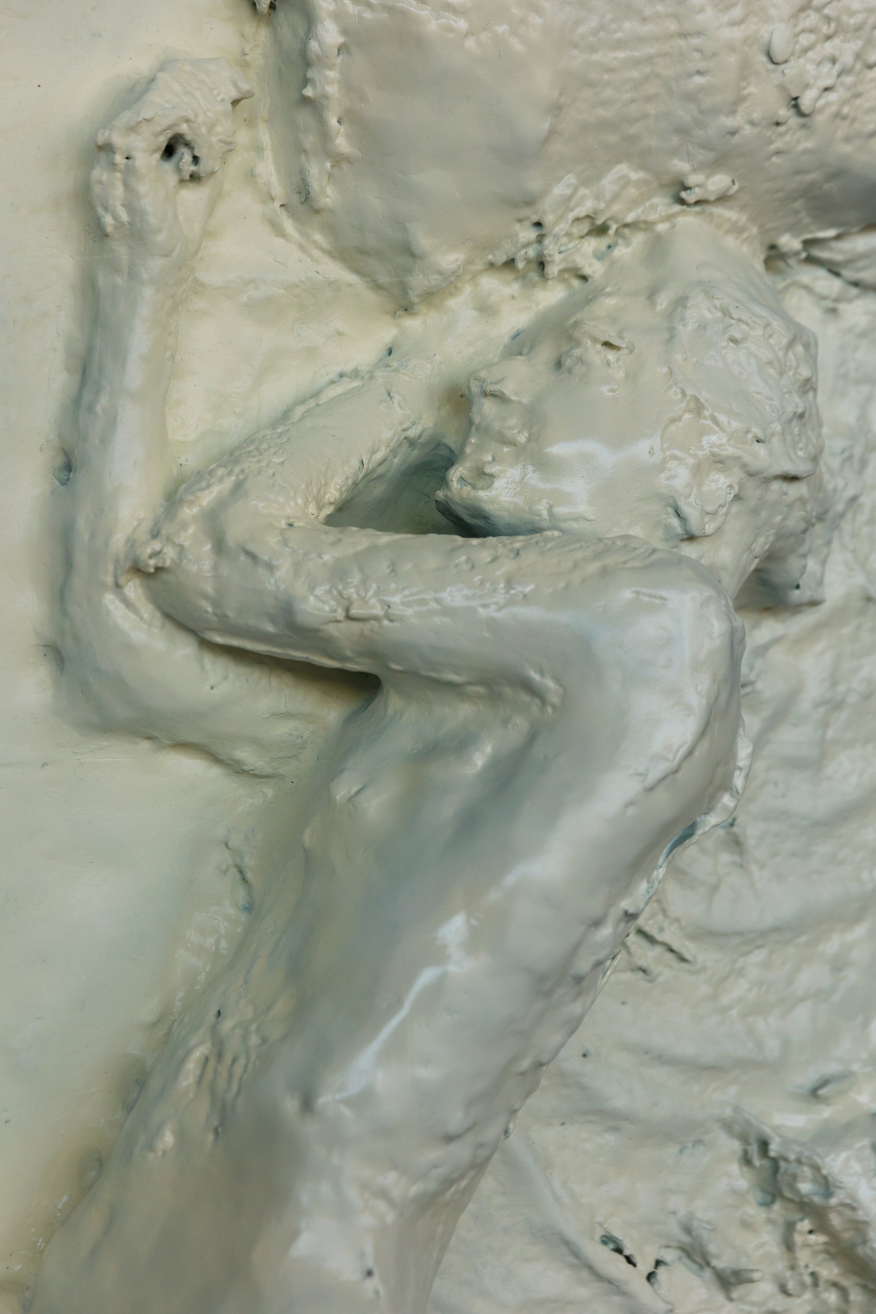Close-up of the relief showing the figure's arm and head against the glossy cream surface