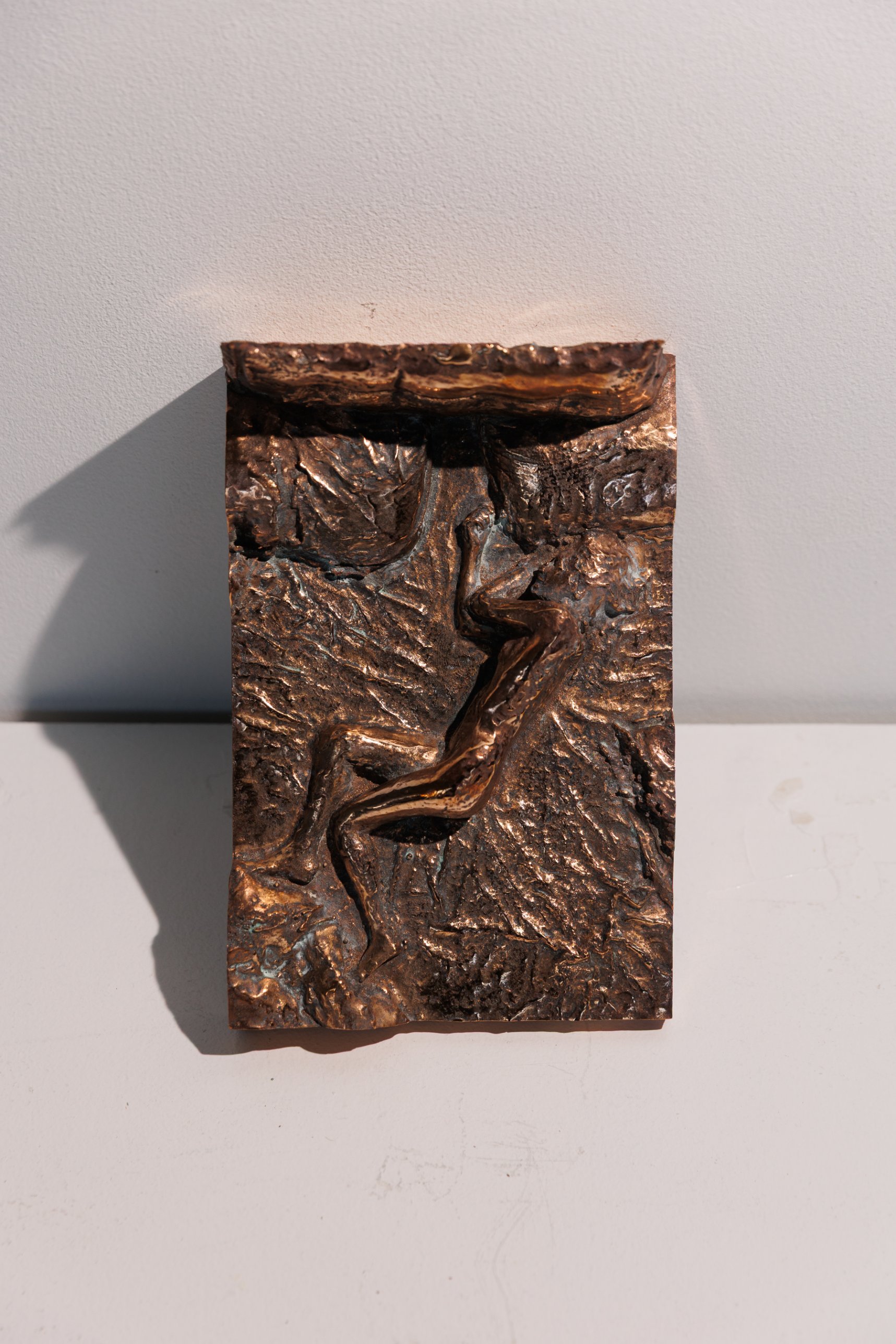 Small bronze relief of a sleeping figure on a bed, leaning against a white wall
